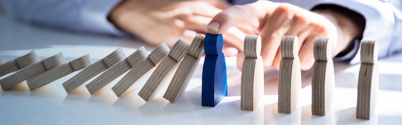 Image of people shaped dominos being held up by a male hand