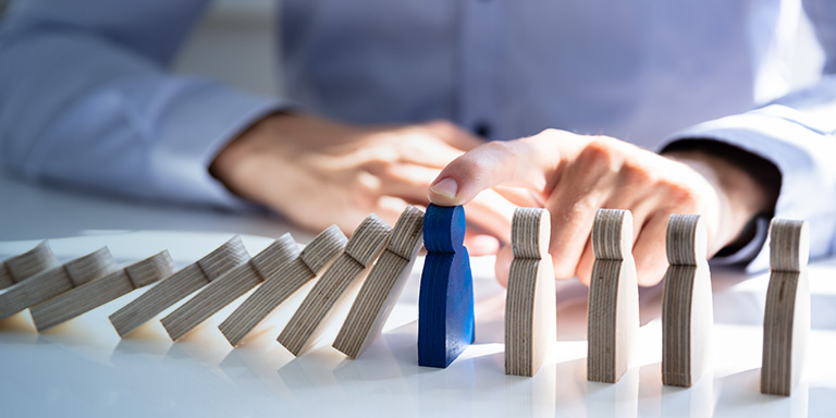 Image of people shaped dominos being held up by a male hand