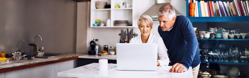 A man and woman looking at a laptop in their kitchen
