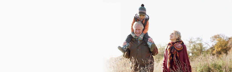 Investing for your children and grandchildren image of an older woman and man with a child on his shoulders walking through a field
