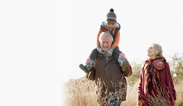 Investing for your children and grandchildren image of an older woman and man with a child on his shoulders walking through a field